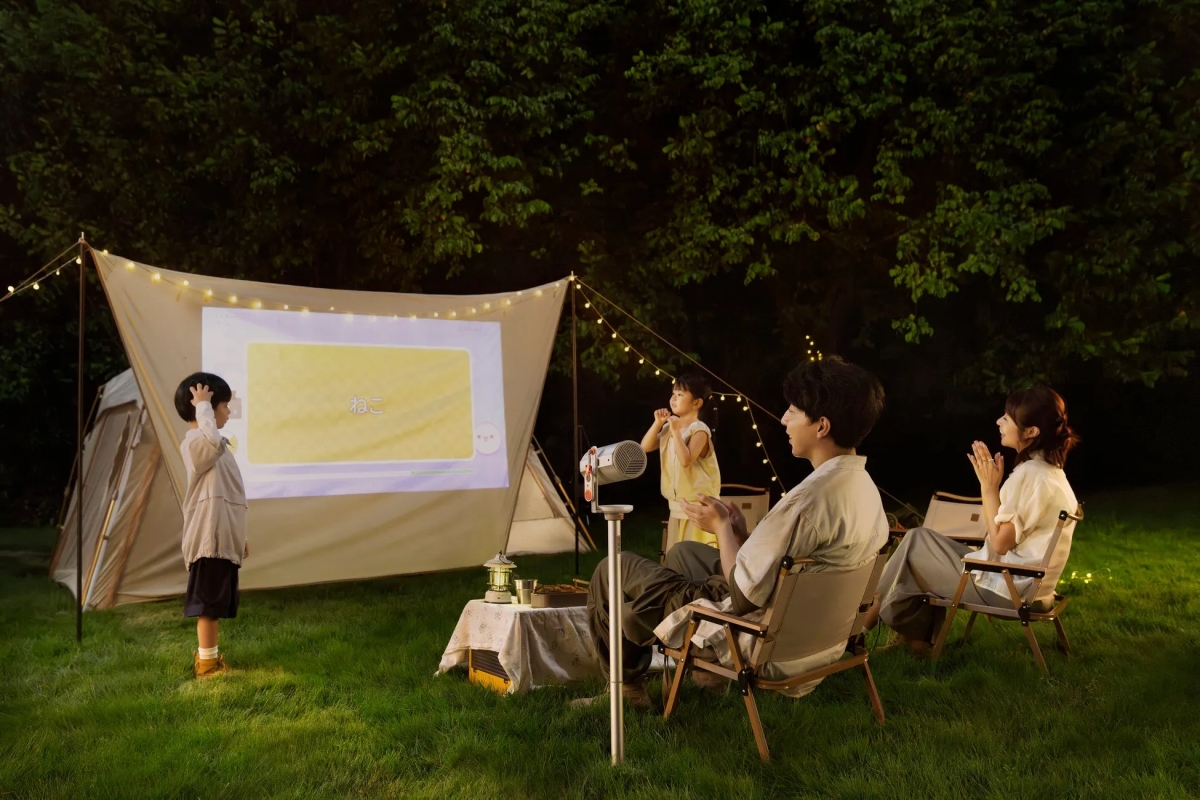 庭で家族がプロジェクターを使って映画を見ている様子。子供たちはスクリーンを見ており、両親は椅子に座って楽しんでいる。