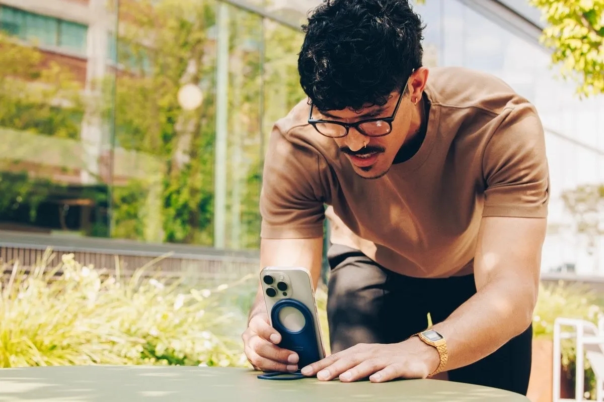 男性が屋外でスマートフォンに何らかのアクセサリーを取り付けている様子。