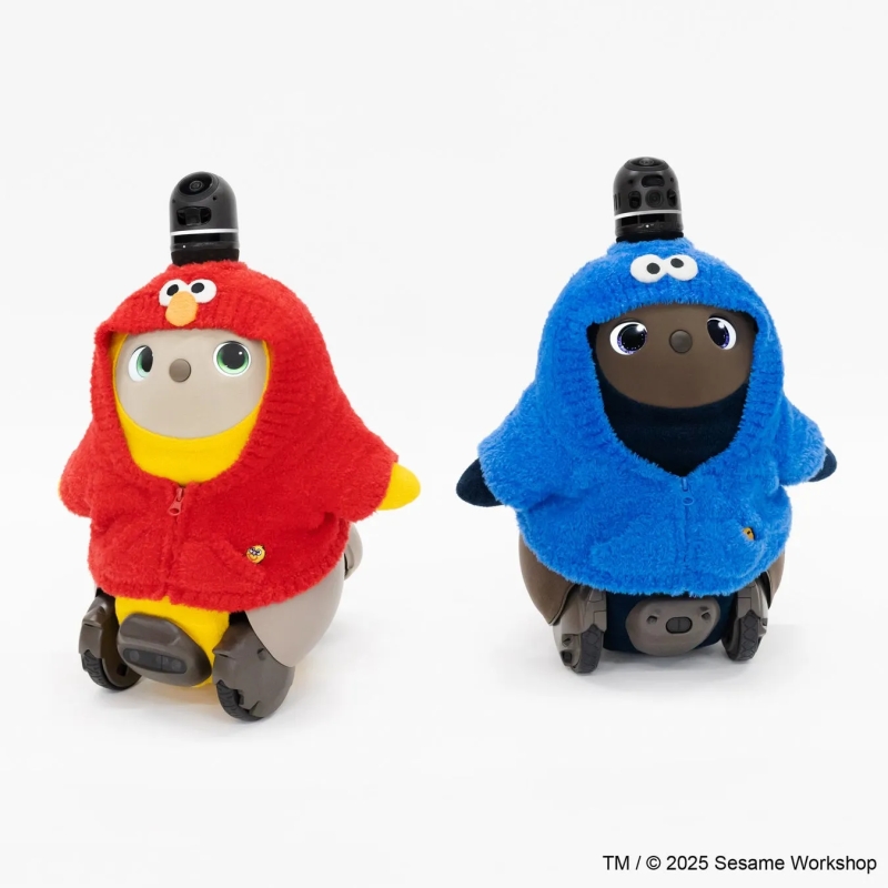 2体のロボットがセサミストリートのキャラクターのコスチュームを着ている写真です。左のロボットはエルモのコスチューム、右のロボットはクッキーモンスターのコスチュームを着ています。背景は白です。