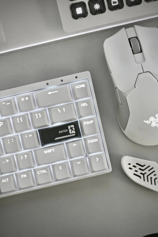 白いキーボード、マウス、マウスパッドが写った写真です。キーボードのEnterキーには、人が出口に向かって歩いているようなアイコンが描かれています。マウスはRazerのものである。