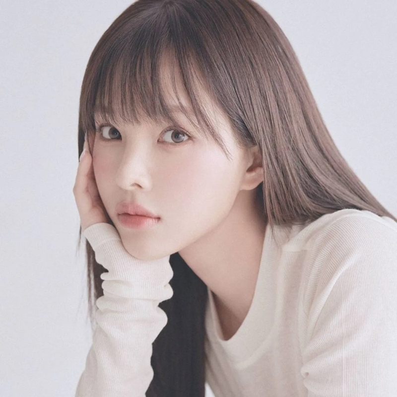 女性のポートレート。長い茶色の髪で、白い服を着て、顔を手に当てている。