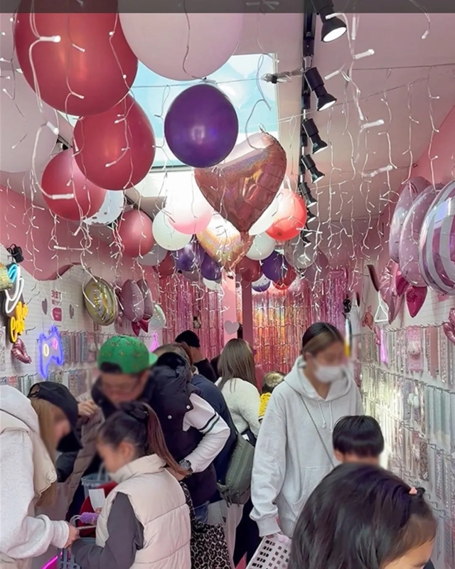 店内には、様々な色の風船や飾り付けが施され、人たちが商品を選んでいる様子。