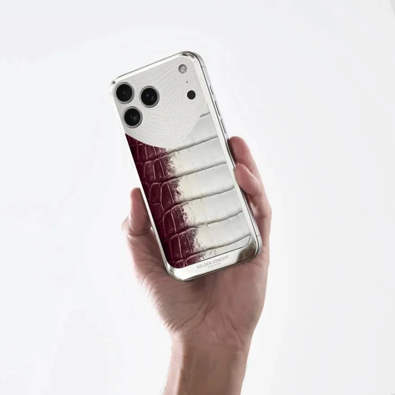 手が高級感のあるスマートフォンケースを握っている画像です。シルバーの金属部分と、赤から白へグラデーションするクロコダイル調の革素材が特徴的なツートンカラーのデザインで、底部には「GOLDEN CONCEPT」のロゴが見えます。