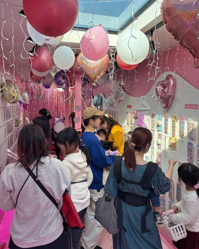 ピンクを基調とした店内で、多くの人が商品を選んでいる様子。天井には様々な形の風船が飾られ、華やかな雰囲気。