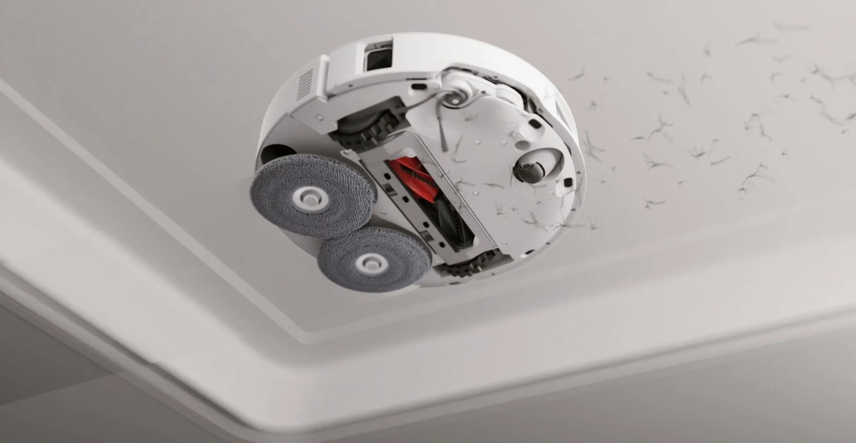 天井を掃除しているロボット掃除機の写真。掃除機は白く、2つの円形の清掃パッドと赤色のブラシが付いている。掃除機は天井に付着したほこりを掃除しているように見える。