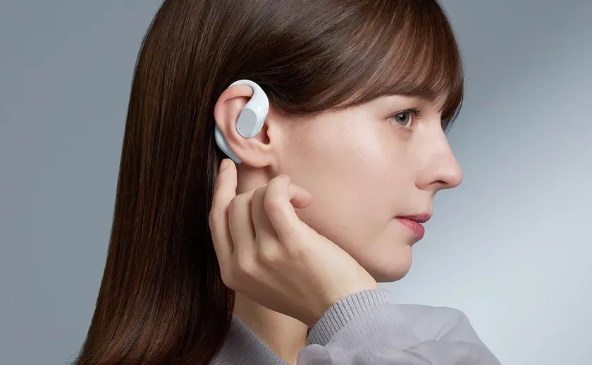 白いオープンイヤー型イヤホンを装着した女性の側面ポートレートです。