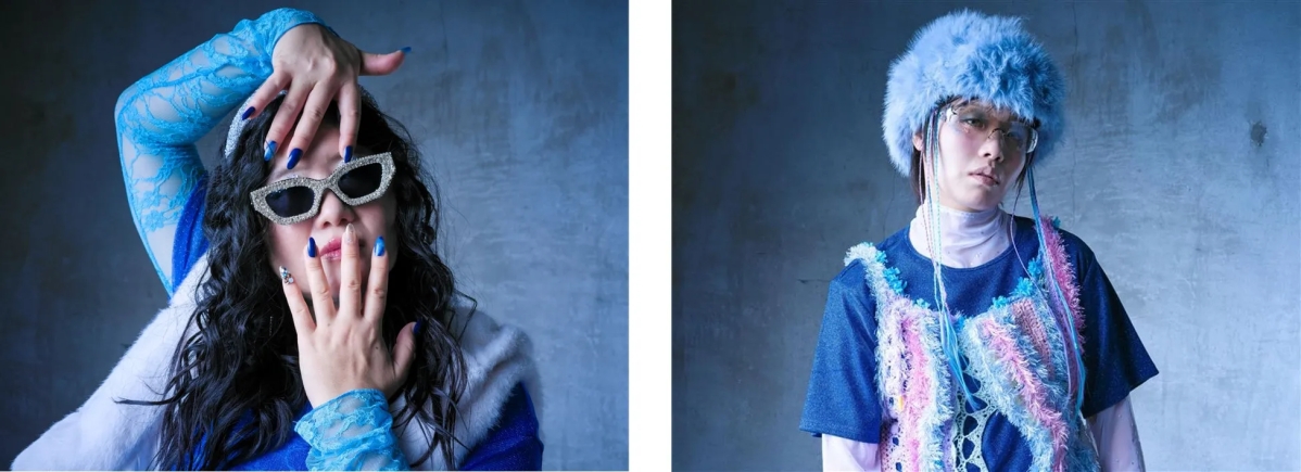 2人の人物が写った写真。左側の人物は、青いレースの袖、キラキラのサングラス、青いネイルをしており、手で顔を覆っている。右側の人物は、青いファーの帽子、メガネ、カラフルな装飾が施されたトップスを着ている。