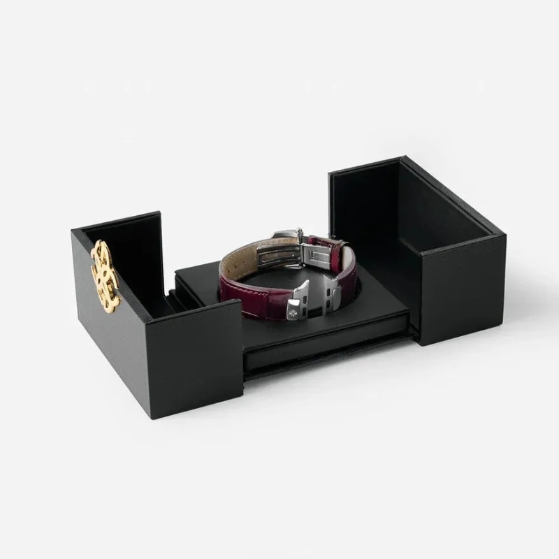 黒い箱に収められたワインレッドのレザー製時計バンドの画像です。バンドはDバックル式の留め金が付いており、箱の蓋には金色のエンブレムが見えます。高級感のあるギフトやアクセサリーのイメージです。