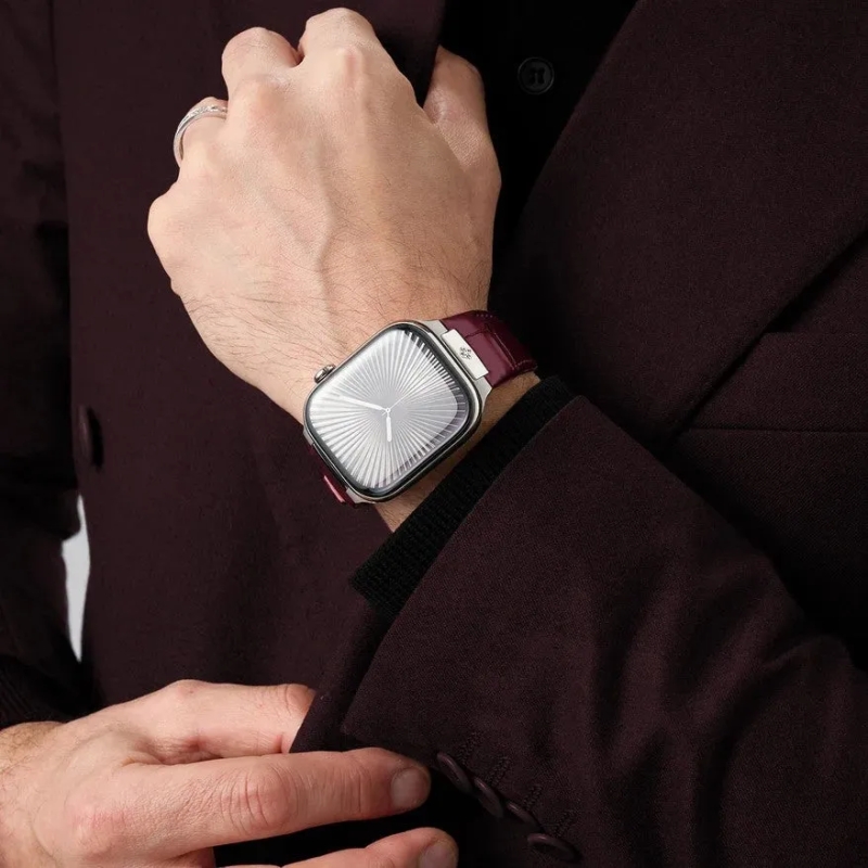 バーガンディ色のスーツジャケットを着た男性の手元が写っています。左手首には、シルバーのケースとワインレッドの革ベルトが特徴的なアナログ表示のスマートウォッチが着用されており、上品な印象を与えています。