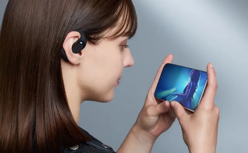 女性がイヤホンを着用し、スマートフォンで音楽ライブ映像を視聴している様子を捉えた画像。