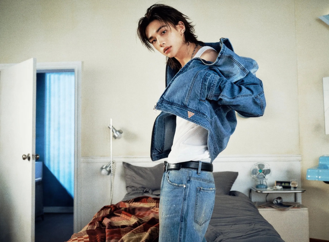 デニムジャケットを着た男性が、ベッドルームでポーズをとっています。