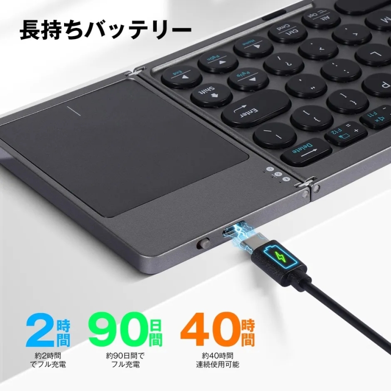 ワイヤレスキーボードの充電中の写真。キーボードはグレーで、右側に丸いキーがあり、左側にはタッチパッドがあります。充電時間は約2時間で、90日間フル充電でき、40時間連続使用可能です。