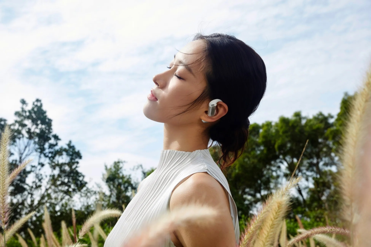 イヤホンをつけた女性が屋外で目を閉じて空を見上げている様子。