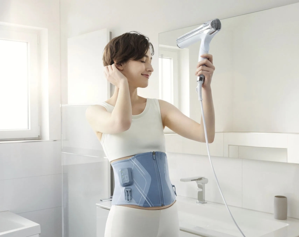 女性が洗面所でドライヤーを使い髪を乾かしている様子。コルセット着用