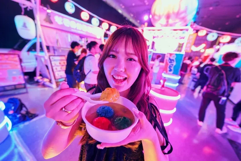 女性がカラフルなデザートを手に持ち、笑顔でカメラを見ている