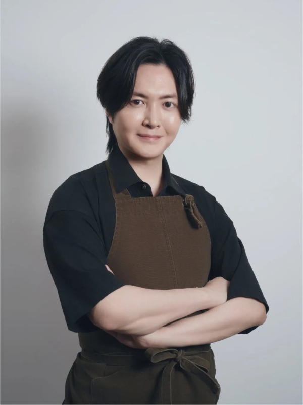 茶色のエプロンを着て腕を組んだ男性のポートレート。